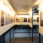 Exposição de fotografias em uma galeria de arte contemporânea, com obras dispostas nas paredes.
