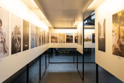 Exposição de fotografias em uma galeria de arte contemporânea, com obras dispostas nas paredes.