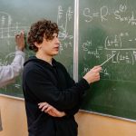 Grupo de estudantes analisa equações matemáticas em um quadro durante atividade em sala de aula.