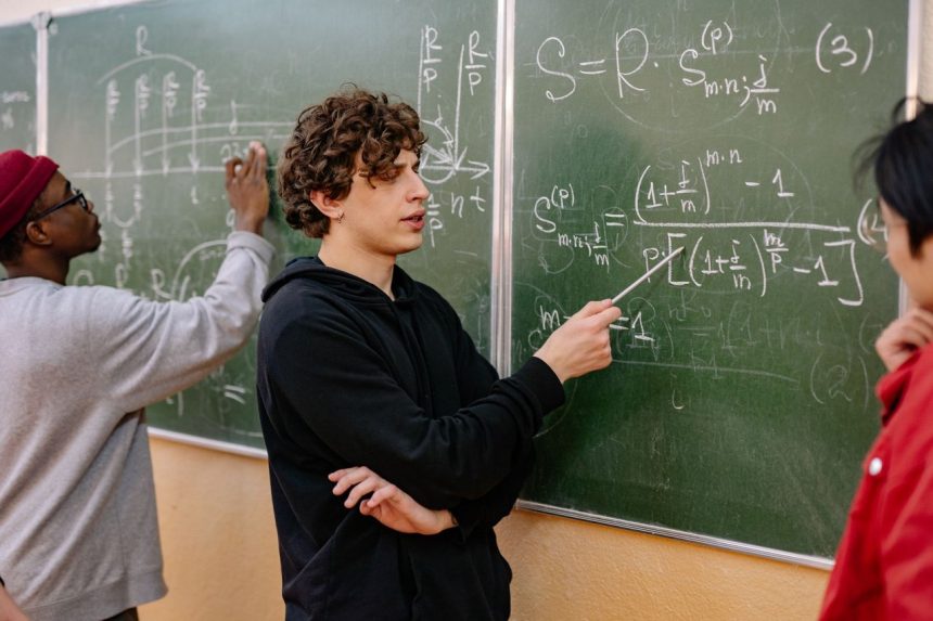 Grupo de estudantes analisa equações matemáticas em um quadro durante atividade em sala de aula.