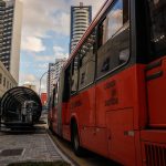 Ônibus vermelho de transporte coletivo em ponto no centro de Curitiba.