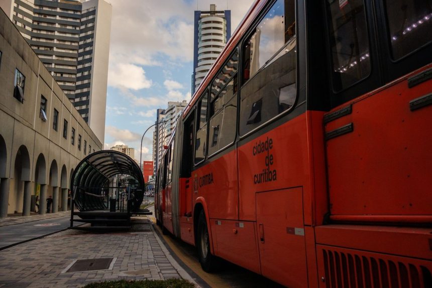 Ônibus vermelho de transporte coletivo em ponto no centro de Curitiba.