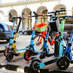 Bicicletas e patinetes elétricos estacionados juntos em uma movimentada rua urbana.