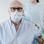 Idoso recebe uma injeção de vacina no braço enquanto é atendido por um profissional de saúde protegido.