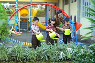 Crianças aprendem a regar plantas com a orientação de uma professora em um espaço verde da escola.