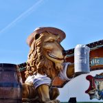 Decoração de festa com uma caneca de cerveja sobre um barril e uma figura de leão ao lado de uma tenda típica de Oktoberfest