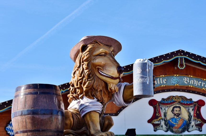 Decoração de festa com uma caneca de cerveja sobre um barril e uma figura de leão ao lado de uma tenda típica de Oktoberfest